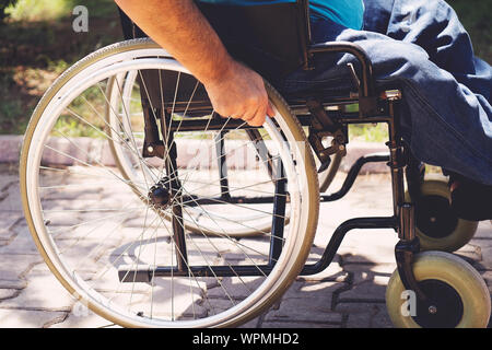 Close up photo of Young disabled man holding wheelchair outside in park Stock Photo