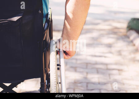 Close up photo of Young disabled man holding wheelchair outside in park Stock Photo