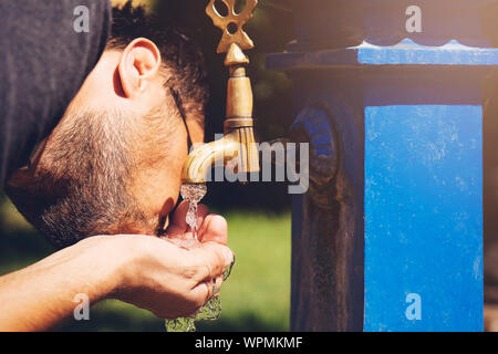 Caucasian young man preparing to drinking water from the retro fountain. Stock Photo