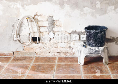 Black dirty bucket and spatula tools and white brick wall. Unfinished room reconstruction. Home repair, improvement. Work in progress. Rebuilding, ren Stock Photo