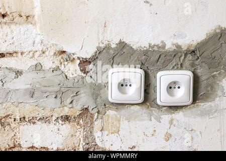 Couple of electric power plug sockets on old white dirty brick wall. Electricity repair and reconstruction concept. Vintage grunge background, home un Stock Photo