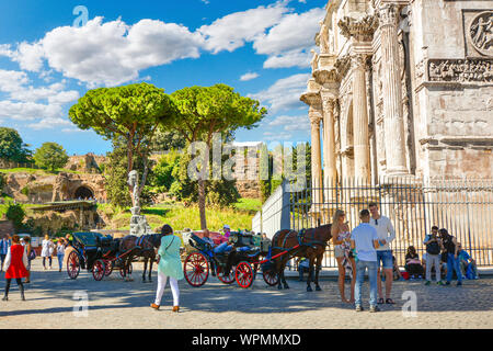 Tourists at the Arch of Constantine near the Colosseum and the Roman Forum with Capitoline Hill in the background as horse and carriages wait for hire Stock Photo