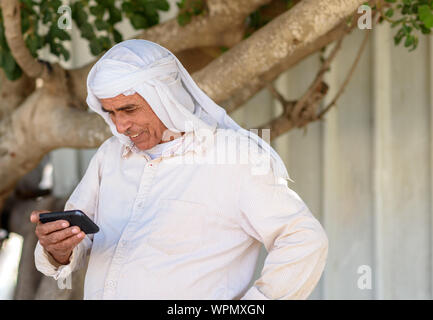 Old Arabic man in traditional clothes outdoor portrait.Smiling Muslim Senior businessman using a smartphone. Stock Photo