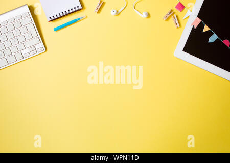 Flat lay style top view of juvenile workspace with tablet, notebook, marker, clothes pegs and keyboard on yellow pastel background. Space for text Stock Photo
