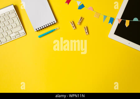 Minimal top view of a youth table desk with laptop, keyboard, notebook, pen and some small clothes pegs. Freelancer workplace concept on yellow backgr Stock Photo