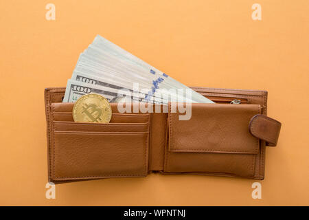 Bitcoin, hundred dollar bills and leather wallet on the orange background. Stock Photo