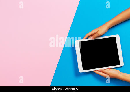Kid hands with tablet computer on pastel pink and blue background Stock Photo
