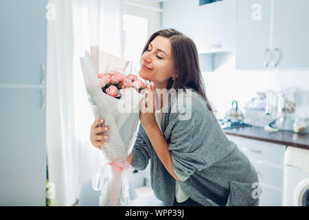 Happy woman smelling bouquet of roses. Housewife enjoying decor and interior of kitchen. Sweet home. Allergy free Stock Photo