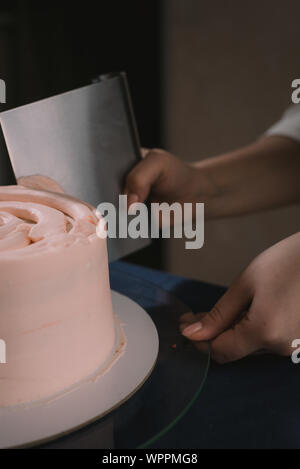 Confectioner aligns the cream with a spatula. The master of cakes lines the cream on a beige wedding cake Stock Photo