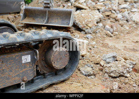 Rubber track of a mini digger in selective focus against background of concrete and earth excavation debris Stock Photo