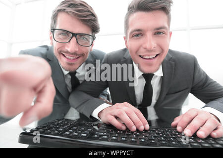 two young businessman are looking into the camera while sitting in the office. One shows the index finger Stock Photo