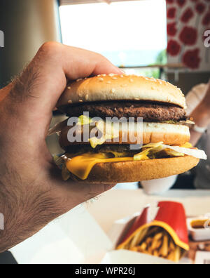 Male hand holding delicious double hamburger admiring the high calorie meat and bun with salad and cheese in between Stock Photo