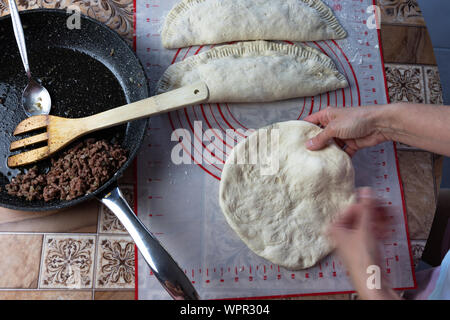 Close up of a woman's hands making dough for homemade bread, empanadas. female baker preparing bread on a silicone baking sheet. frying pan with grinn Stock Photo