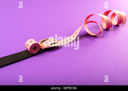 pink spiral measuring tape on a black waist belt on a violet background, the concept of excess weight and weight loss Stock Photo