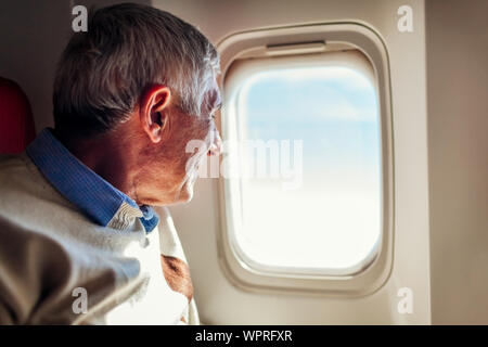 Senior man looking at airplane window. Passenger sitting in comfortable business class seat and feeling scared of flights Stock Photo