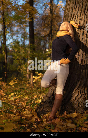 The girl rests on a tree and is photographed at sunset in cowboy clothes, brown boots Stock Photo