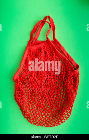Red shopping mesh bag on green background. Zero waste concept and plastic free concept. Stock Photo