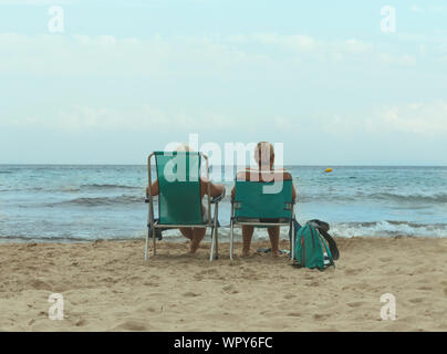 Elderly couple sitting on the beach facing the sea. Benidorm, Alicante, Spain, August 20, 2019 Stock Photo