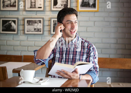 Young man talking on a mobile phone and reading a book in a restaurant Stock Photo