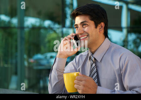 Businessman having a cup of coffee and talking on mobile phone Stock Photo