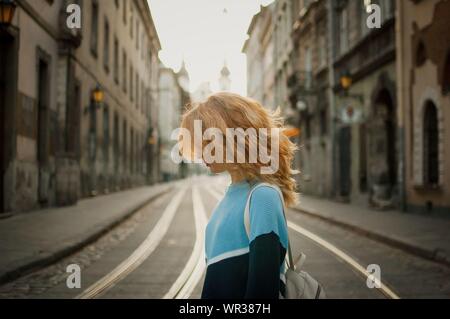 Side view of beautiful young adult girl tourist enjoying her trip early in the morning in empty city in Europe on street with tramway background Stock Photo