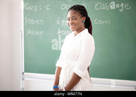 African-American teacher smiling while standing near blackboard Stock Photo