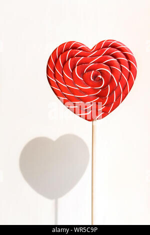 Heart shaped sweet lollipop on white wall background with shadow.  Stock Photo