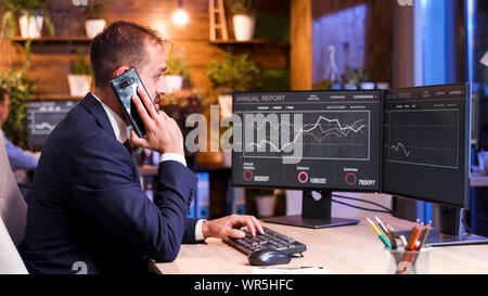 The manager speaks on the phone while analyzing some graphics on the monitor. Two screens Stock Photo