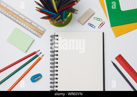 Empty spiral notebook with white page and multicolored stationery on a blue table. Workplace with notepad on colored background. Sketch-book for input Stock Photo