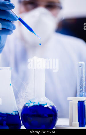 Female scientist in protection equipment using a pipette with dropping blue solution in research laboratory. Stock Photo