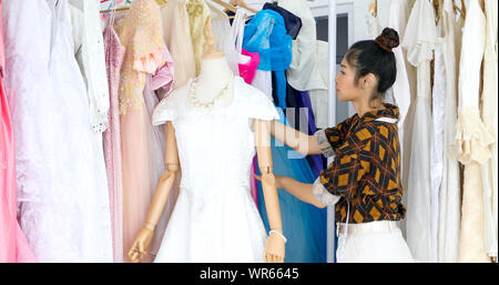 Small Business of Asian women Fashion Designer Working and using smart phone and tablet With Wedding Dresses at at clothing store Stock Photo