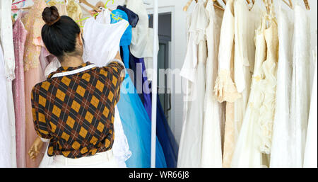 Small Business of Asian women Fashion Designer Working and using smart phone and tablet With Wedding Dresses at at clothing store Stock Photo