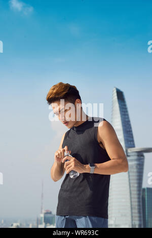 Young sports man opens a bottle of water teeth. The concept of sport and a healthy lifestyle. Stock Photo