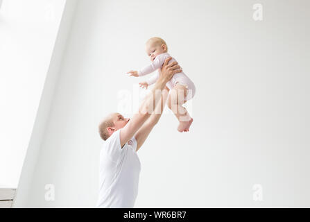 Father lifting baby girl. Happy father picks up and throws his lifting a small child. Home atmosphere, happy family laughing baby. Stock Photo