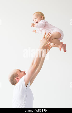 Father lifting baby girl. Happy father picks up and throws his lifting a small child. Home atmosphere, happy family laughing baby. Stock Photo