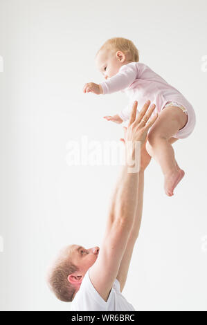 Father lifting baby girl. Happy father picks up and throws his lifting a small child. Home atmosphere, happy family laughing baby. Stock Photo