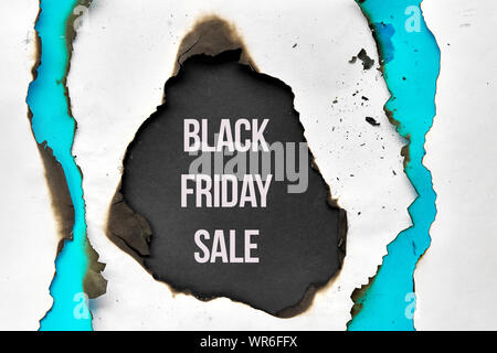 Text 'Black Friday Sale' in burnt hole in white and turquoise paper with burned edges, flat lay on black paper Stock Photo