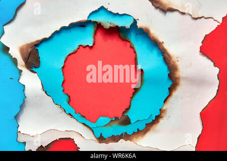 Hole burned though white, red and cyan or turquoise color paper. Abstract flat lay paper pattern with copy-space. Stock Photo