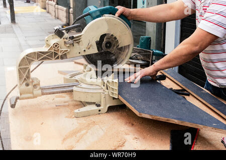 Male carpenter hands cutting laminated wood panels with a circular saw in the street. Stock Photo