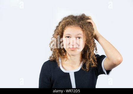 Confused young girl scratching her head looking frustrated over white background. Human facial expression, sign symbol body language. Stock Photo