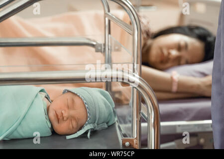 Newborn baby laying in crib with his mother lying on bed side