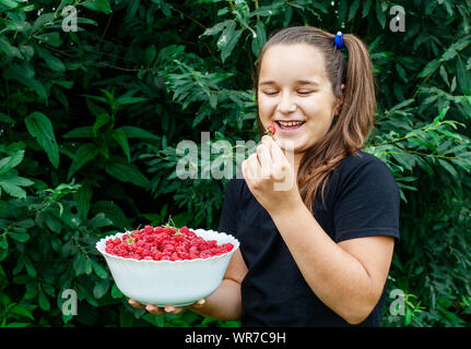 beautiful teen girl holding a bowl of raspberries in the garden closeup on summer day Stock Photo