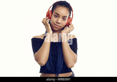 Portrait of beautiful african brunette teenage girl with dreadlocks listening music via wireless headphones isolated on studio background Stock Photo