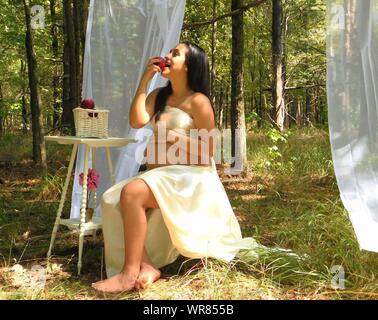 Pregnant Woman Eating Apple While Sitting In Forest
