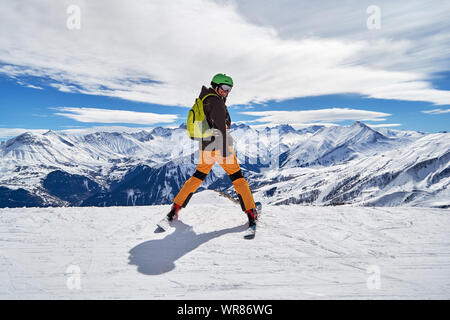 Man skier smiling and posing with a beautiful winter mountain panorama in Les Sybelles ski domain, France, on a sunny day with blue sky and white clou Stock Photo