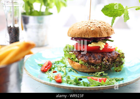 Burger with a grilled beef cutlet, tomato, cucumber, lettuce and sauce served on a plate. Stock Photo