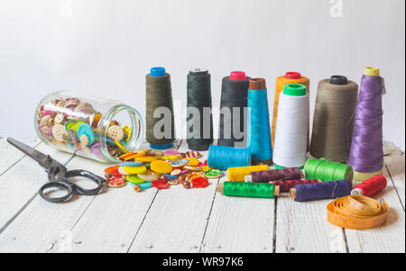 Sewing material (sewing buttons ,sccissors , threads) on old white table with white background Stock Photo