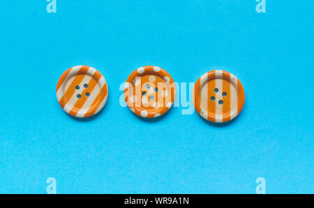 Three Various orange sewing buttons on blue background. Stock Photo