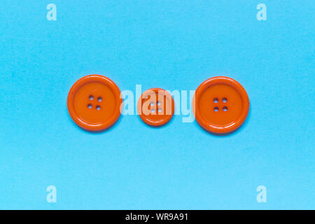 Three Various orange sewing buttons on blue background. Stock Photo