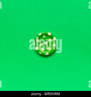 Single green sewing button with dots on green  background. Stock Photo